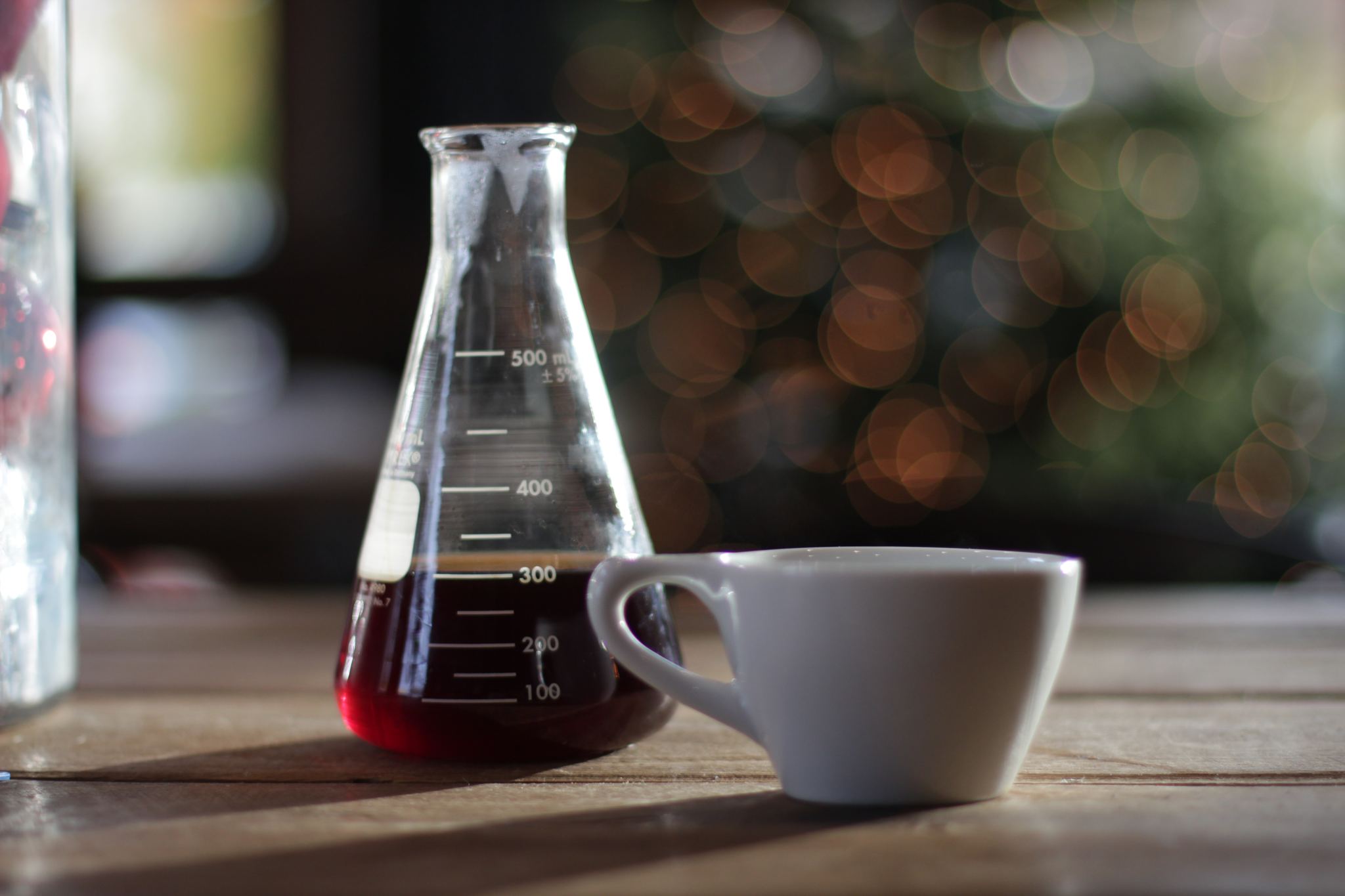 Kona coffee served in a lab beaker and ceramic cup on a wooden table with a blurred background.