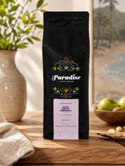 Black coffee bag with 'Paradise Coffee Roasters' branding on a wooden surface.