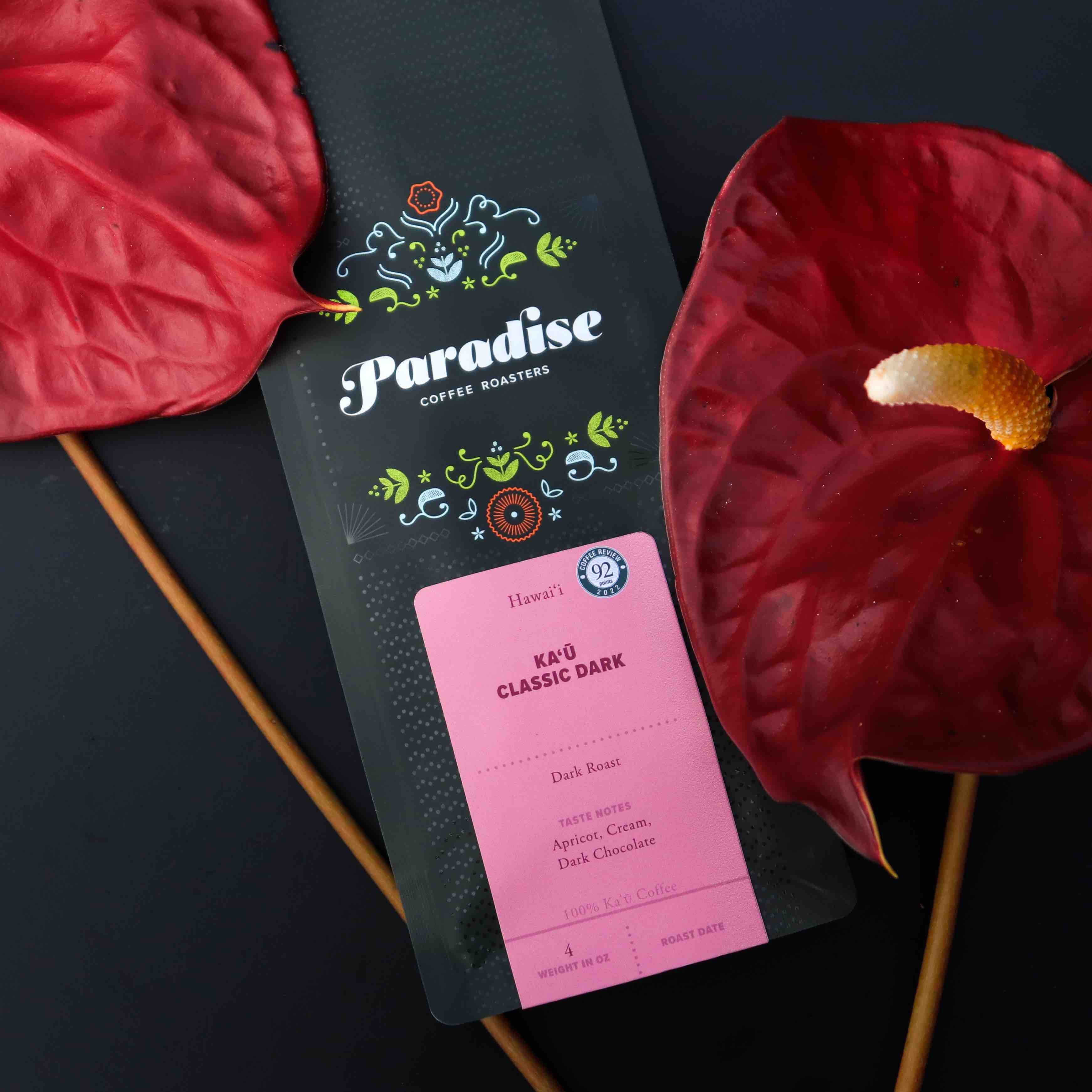 Kaʻū Classic Dark Roast bag  next to red flowers– specialty Hawaiian coffee from Hawaiʻi Island