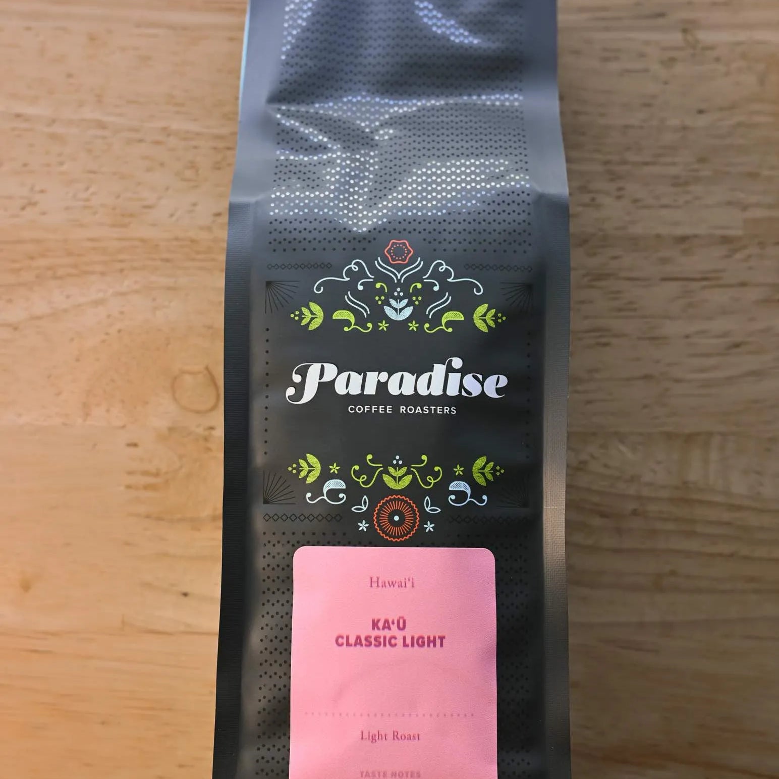 Paradise Roasters Kaʻu Classic Light coffee bag, 12oz, showing pink label with tasting notes Wildflower Honey, Magnolia, and Meyer Lemon