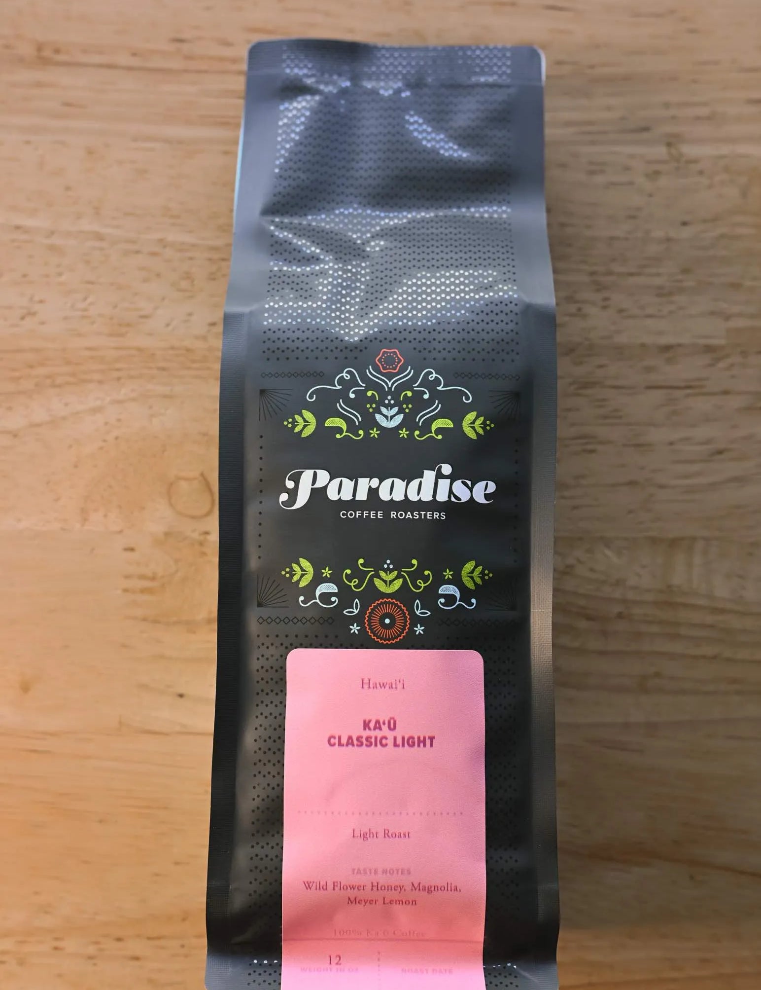 Paradise Roasters Kaʻu Classic Light coffee bag, 12oz, showing pink label with tasting notes Wildflower Honey, Magnolia, and Meyer Lemon