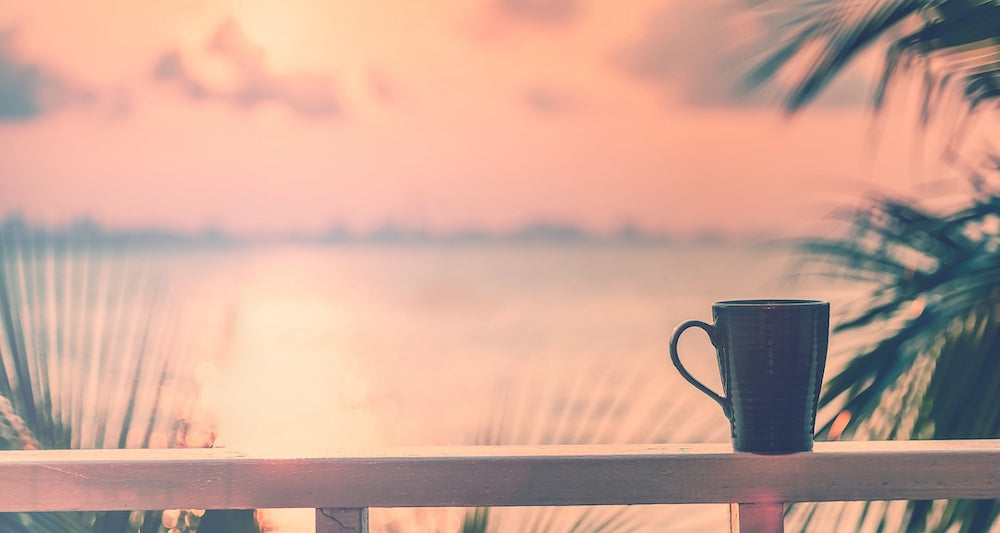 Coffee mug on a wooden ledge with a blurred sunset and palm trees in the background