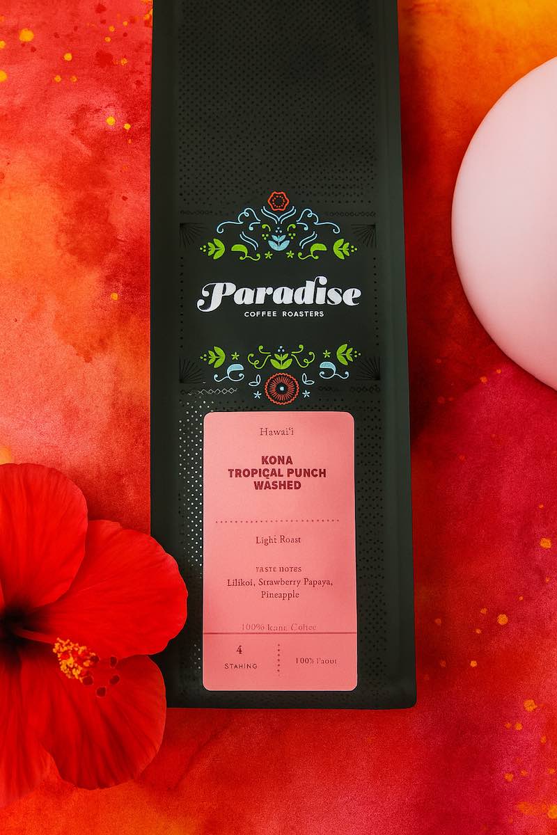 Paradise Coffee Roasters Kona Tropical Punch coffee bag on a red background with a red flower.