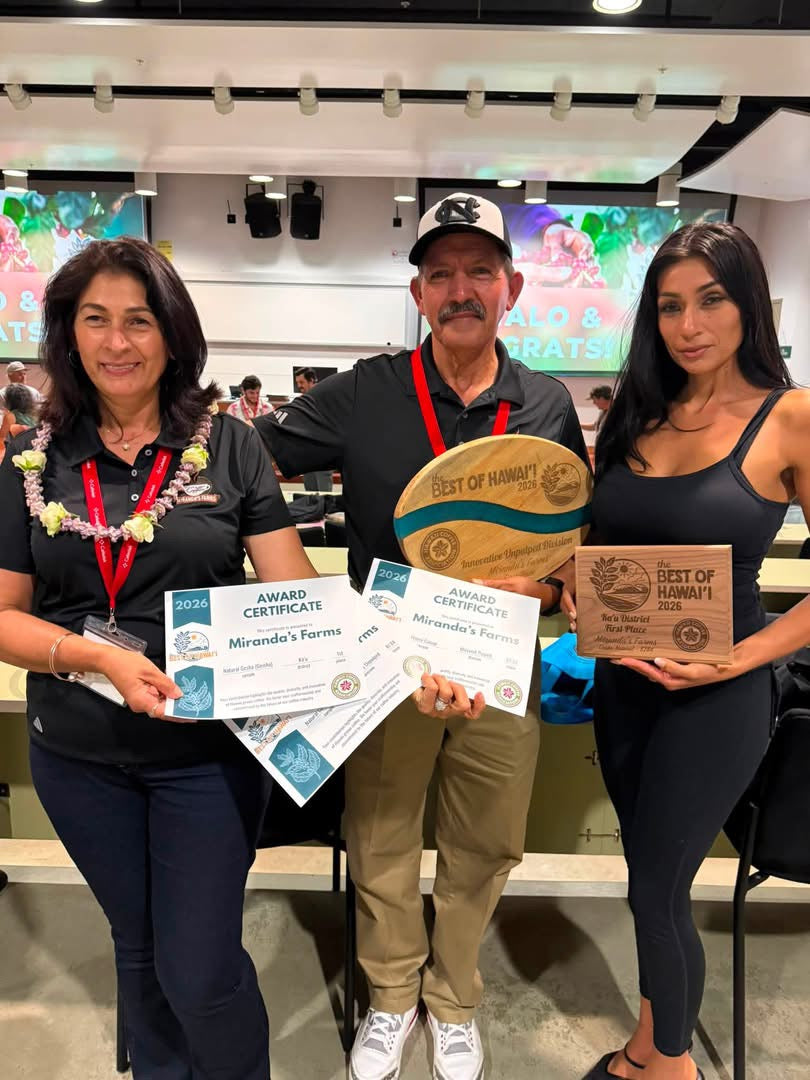 Miranda family standing together indoors, each holding award certificates and plaques. The center person holds a large round wooden plaque reading 'Best of Hawaii,' while the two women on either side hold smaller rectangular plaques and certificates.