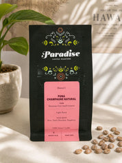 Paradise Coffee Roasters Puna Champagne Natural coffee bag with coffee beans on a light surface.